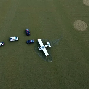Crash site of a small biplane in a rural area of Bullitt County, with emergency responders present.